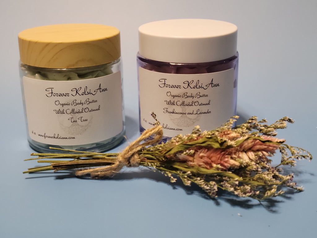 Two jars of Forever Kelsie Ann organic body butter with a bundle of dried flowers on a blue background.