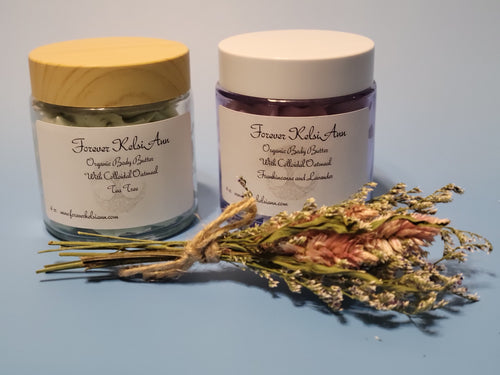 Two jars of Forever Kelsie Ann organic body butter with a bundle of dried flowers on a blue background.