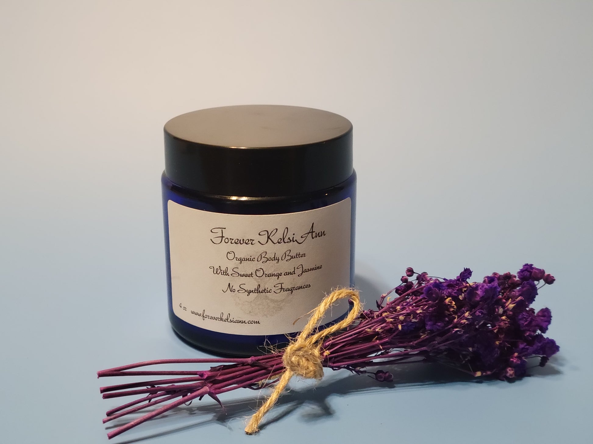 Jar of Forever Kelsi Ann organic body butter with lavender flowers on a light blue background