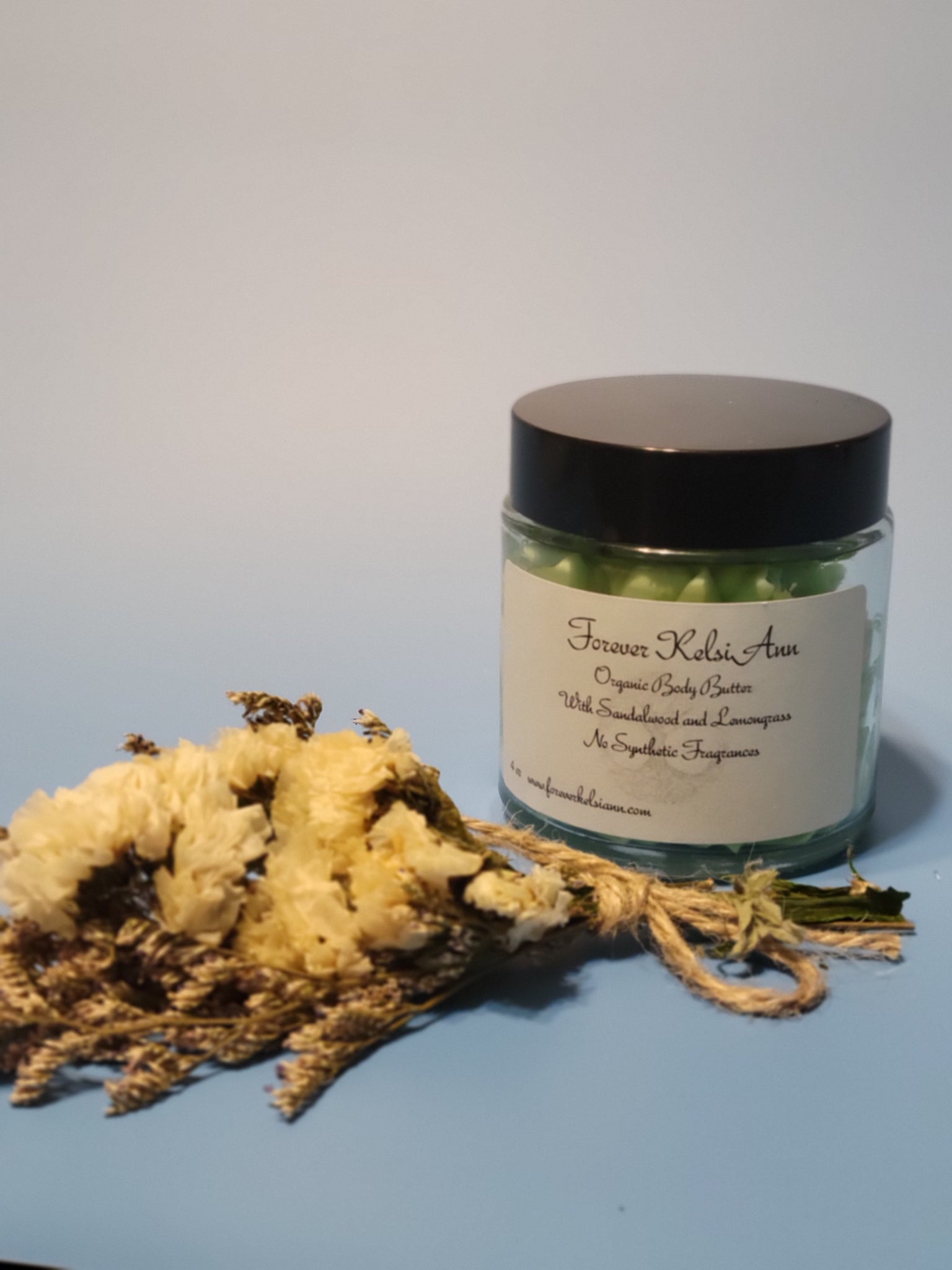 Jar of Forever Kelsi Ann organic Sandalwood and Lemongrass body butter with a decorative rope on a light blue background