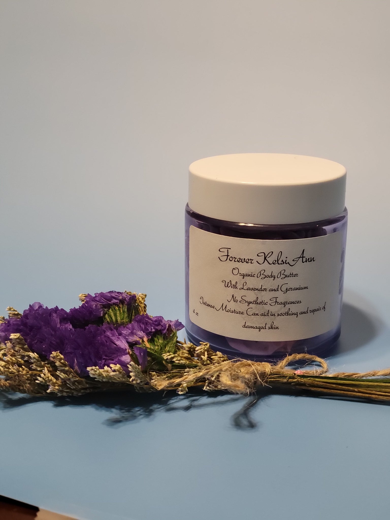 Jar of Forever Kelsi Ann Lavender and Geranium body butter and dried lavender flowers on a light blue background