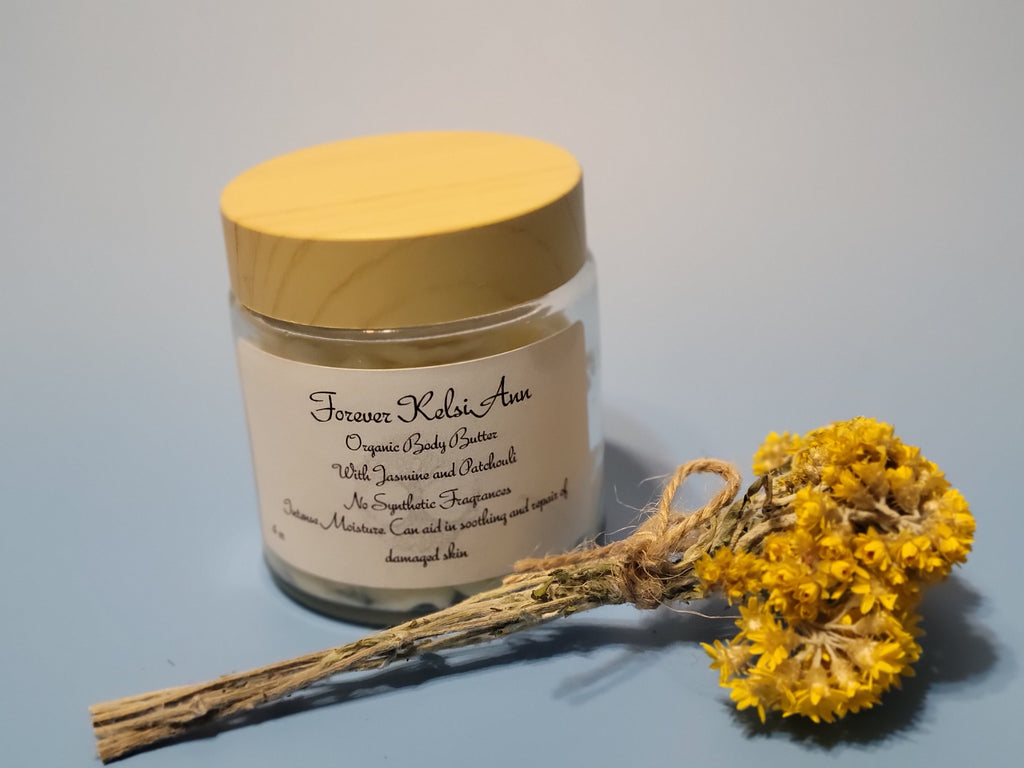 Jar of organic Forever Kelsi Ann Jasmine and Patchouli body butter with a yellow lid and a dried flower on a light blue background