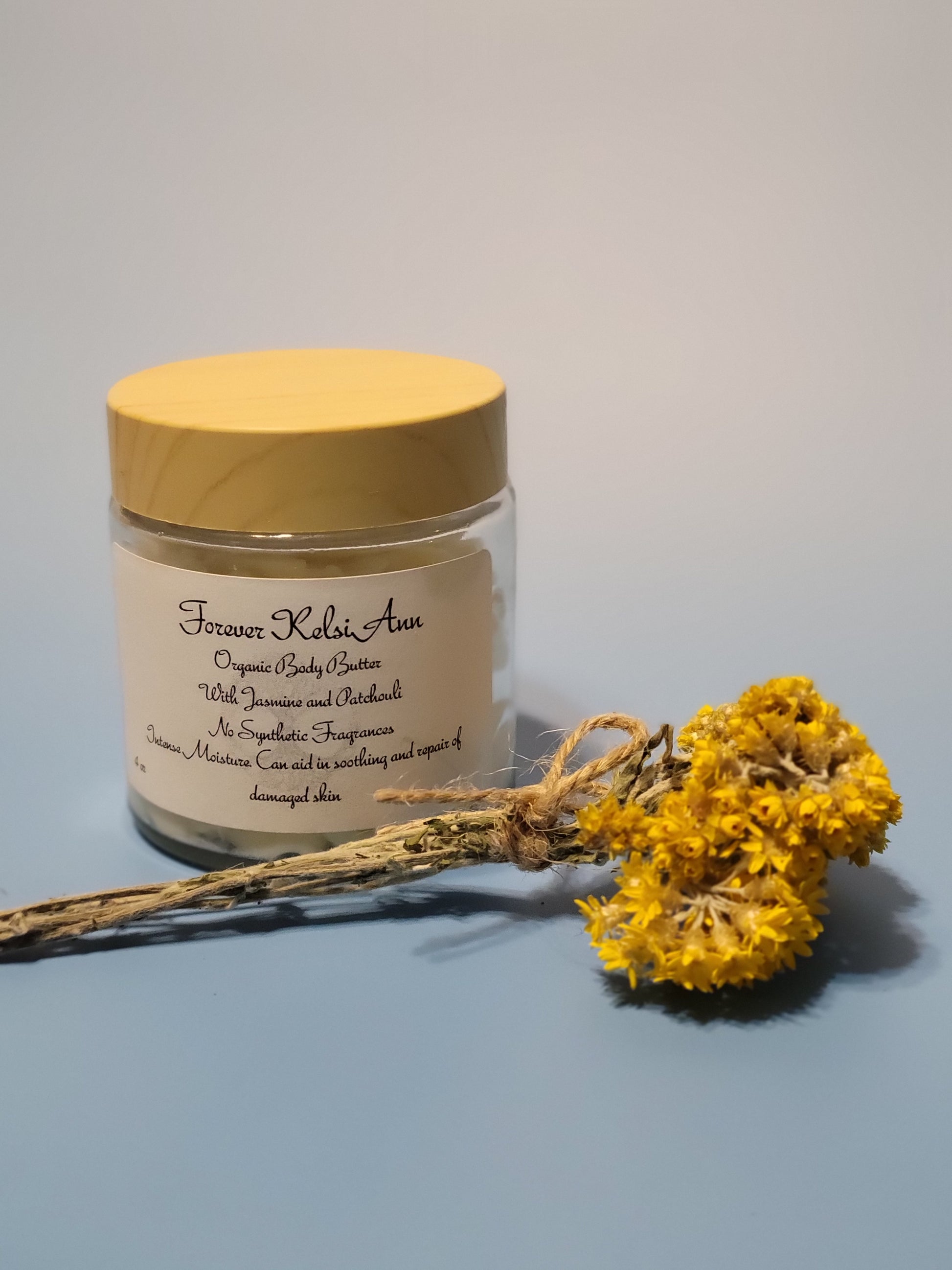 Jar of Forever Kelsi Ann organic Jasmine and Patchouli body butter with a yellow flower on a light gray background