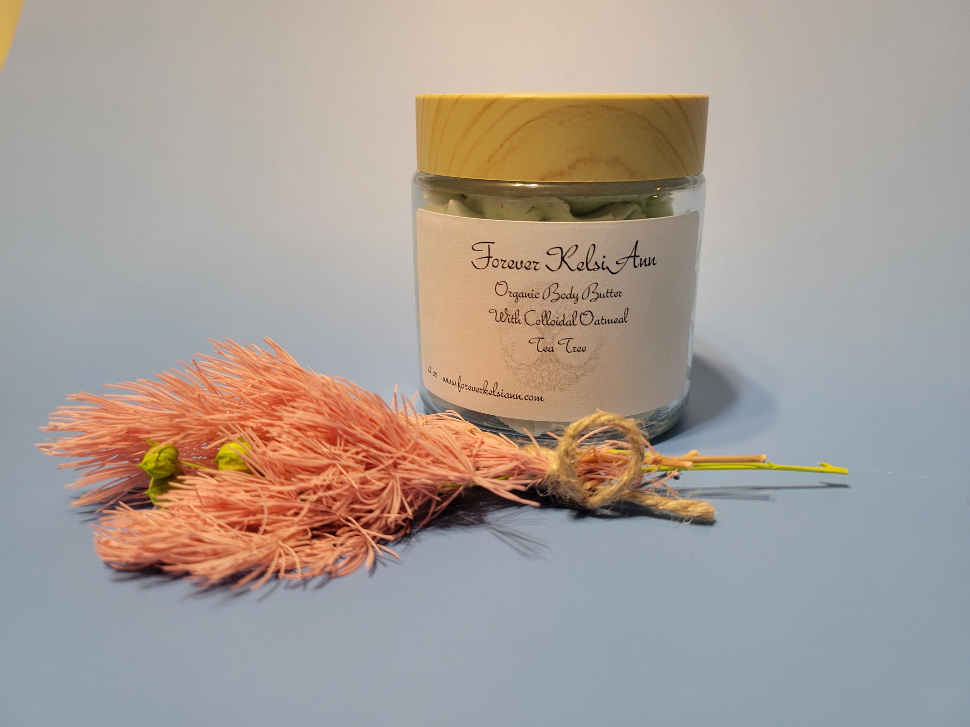 Jar of organic Colloidal Oatmeal body butter infused with Tea Tree Oil, with a pink tassel and dried flowers on a light background
