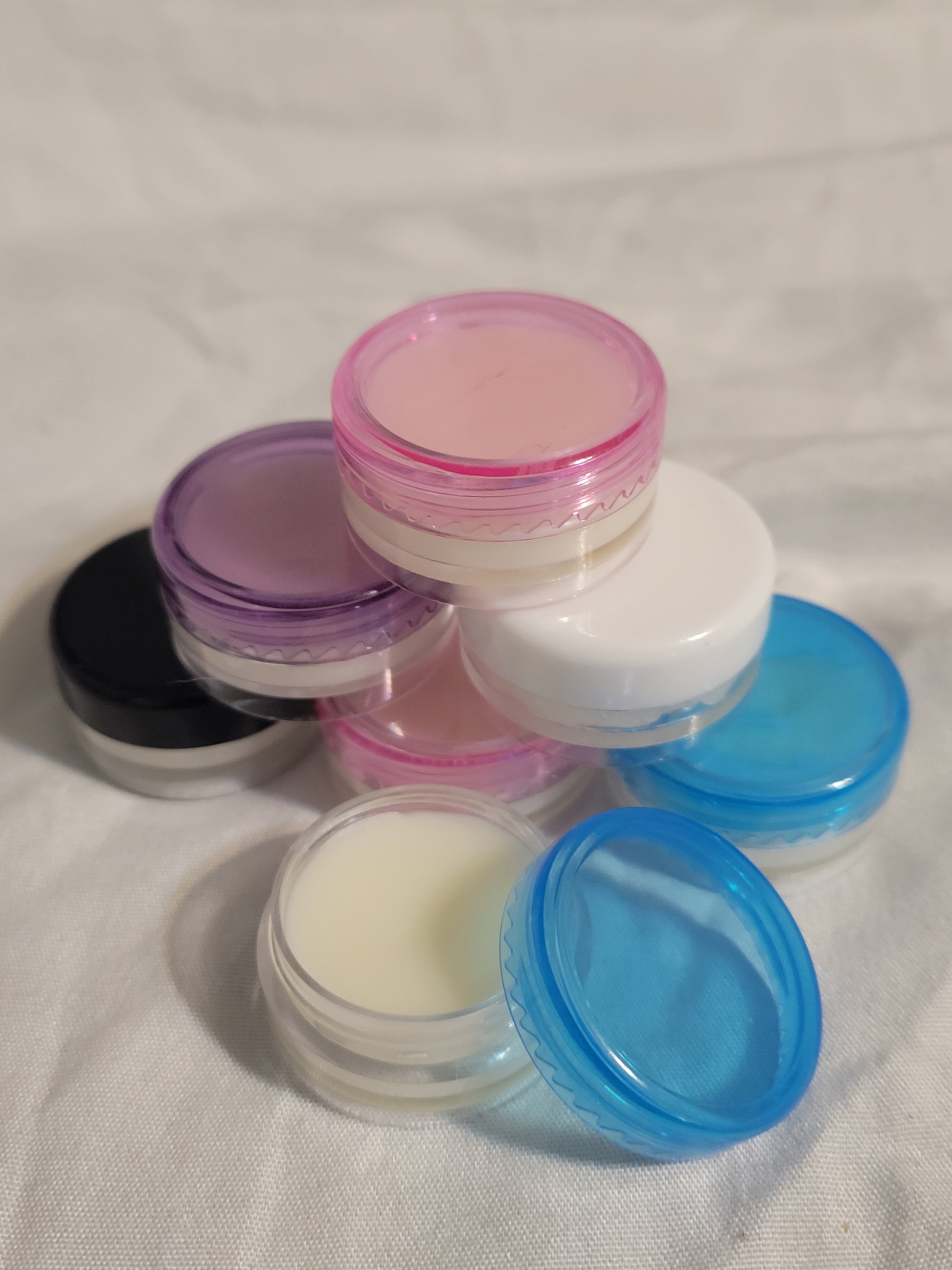 Four small containers of organic lip balm with colorful lids on a white fabric background