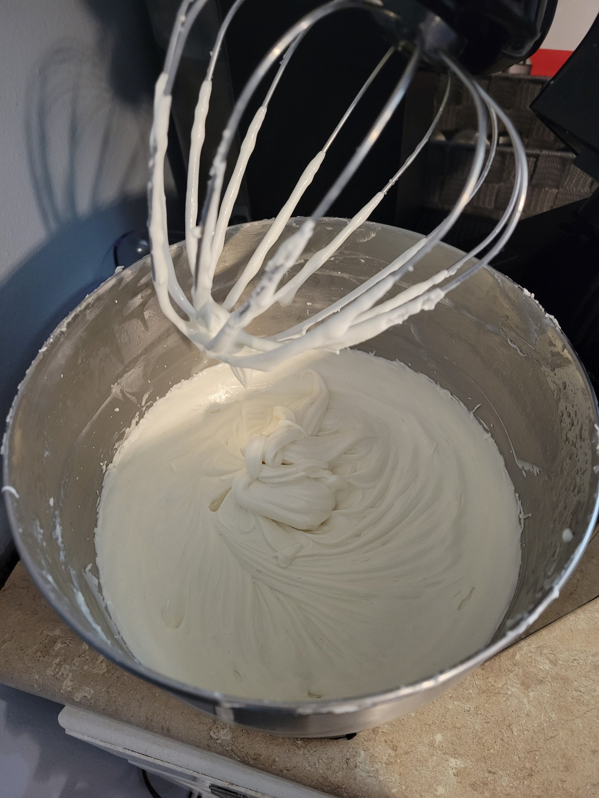 Bowl of whipped body butter with a whisk attachment on a kitchen counter